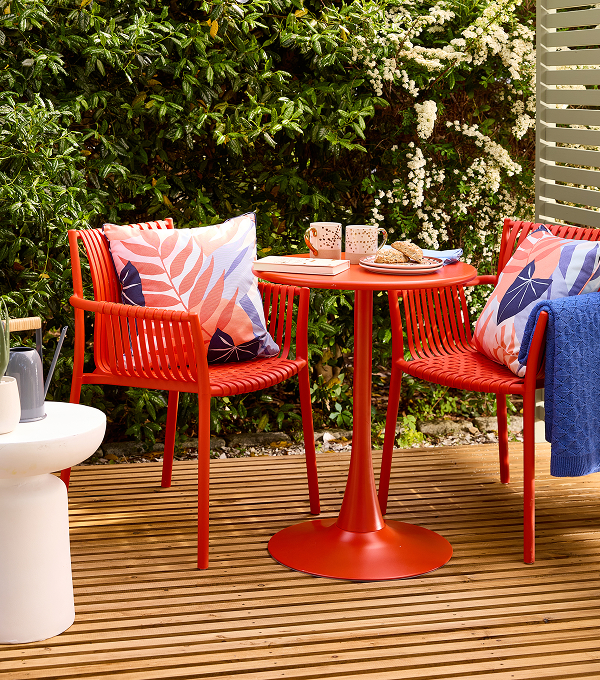 A garden with bold tableware, printed cushions and a bright blue throw.
