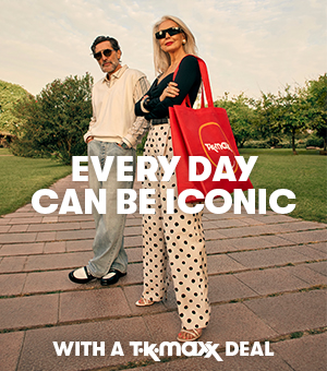 A woman and man both stylishly dressed in a park and holding red TK Maxx shopping bags.