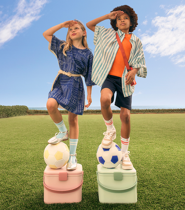 Two kids in stylish outfits, with footballs under their feet, stood on podiums. 