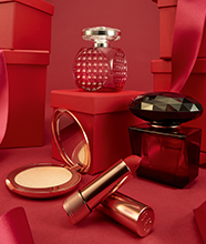 A selection of perfumes and makeup in gleaming glass bottles and golden packaging.