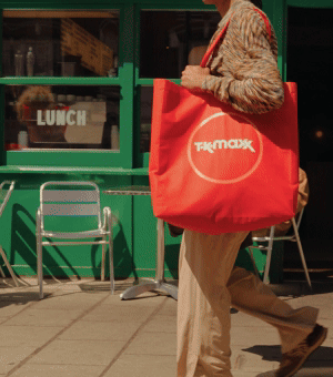 Woman walking wearing stylish designer outfit and holding red TK Maxx bag.